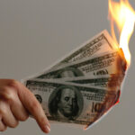 hand holding money lit on fire