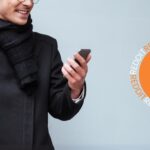 Man with glasses wearing a black coat and black scarf holding a phone