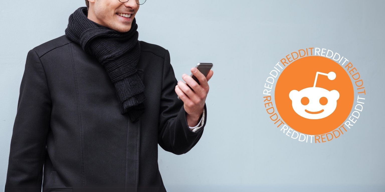 Man with glasses wearing a black coat and black scarf holding a phone