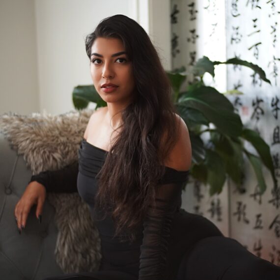 black haired woman Jasmine Sherni with black dress sitting on a couch