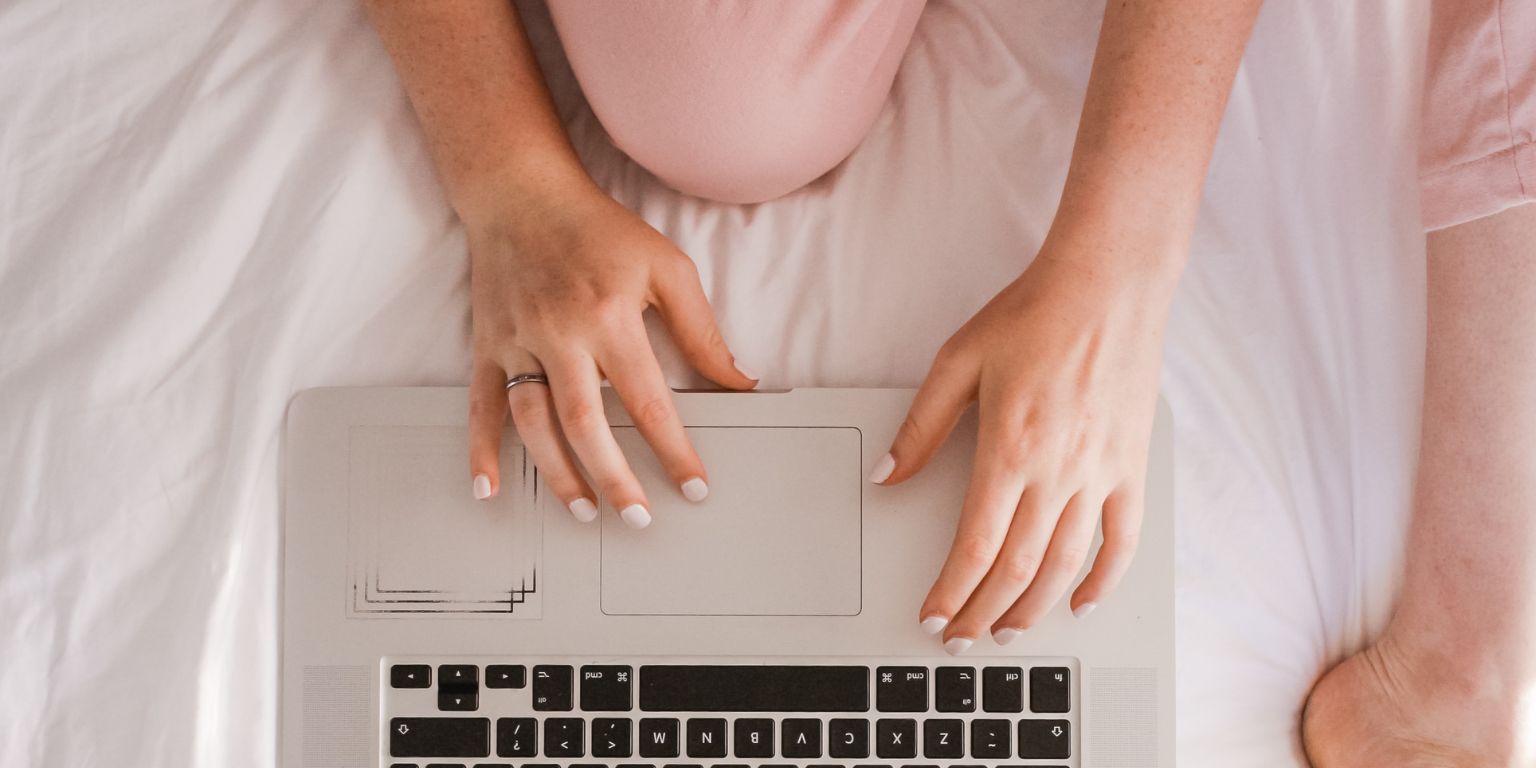 Woman wearing pink pijamas sitting in bed with her laptop