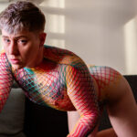nonbinary person bending over wearing rainbow-colored fishnet suit